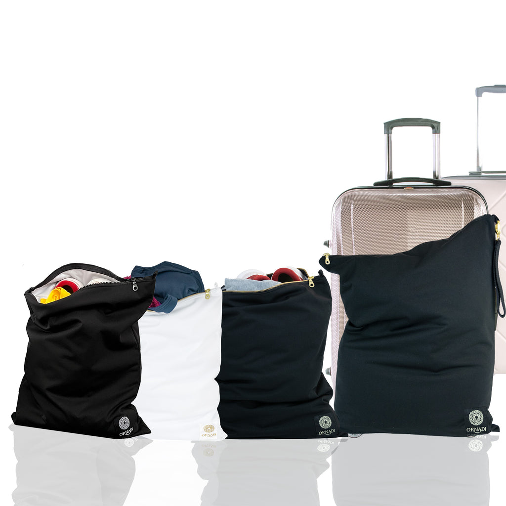 Black and white Ornadi travel laundry bags packed with clothes and swimsuits next to a suitcase on a white background